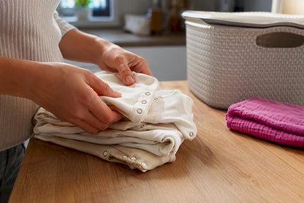 Handen die rompertjes sorteren naast een wasmand